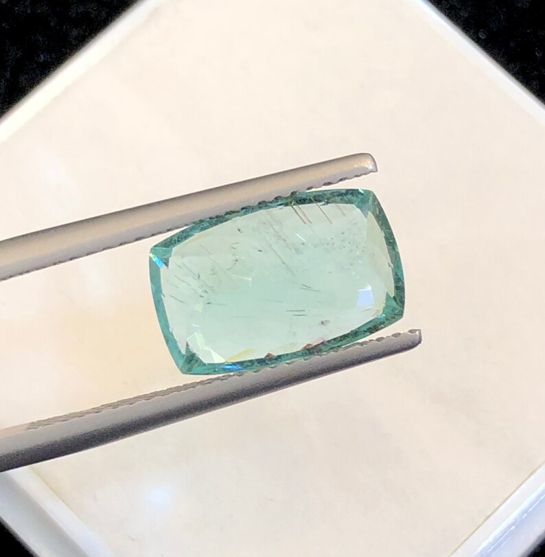 May include: A light green gemstone with a rectangular shape, held in tweezers.