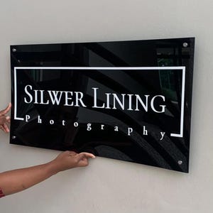 Peut inclure: Une enseigne en acrylique noire avec des lettres blanches qui disent "SILVER LINING Photography".
