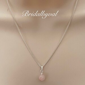 May include: A delicate silver chain necklace with a single, light pink gemstone pendant.