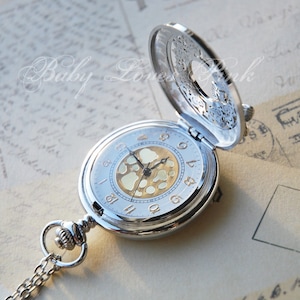 May include: Silver pocket watch with a gold face and a decorative openwork design on the back. The watch has a chain attached.