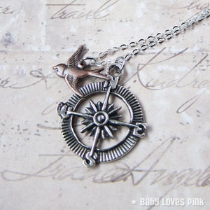 May include: Silver compass necklace with a copper-toned bird charm. The compass features a starburst design and a silver chain.
