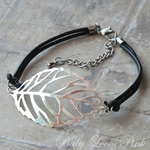 May include: A silver leaf charm bracelet with a black leather cord. The charm is a delicate, openwork design.