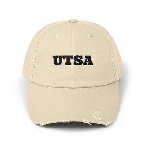 Può includere: Cappellino da baseball beige usurato con la scritta nera "UTSA" sul davanti. Il cappellino ha una visiera curva e un aspetto leggermente usurato, con dettagli intenzionali sui bordi.