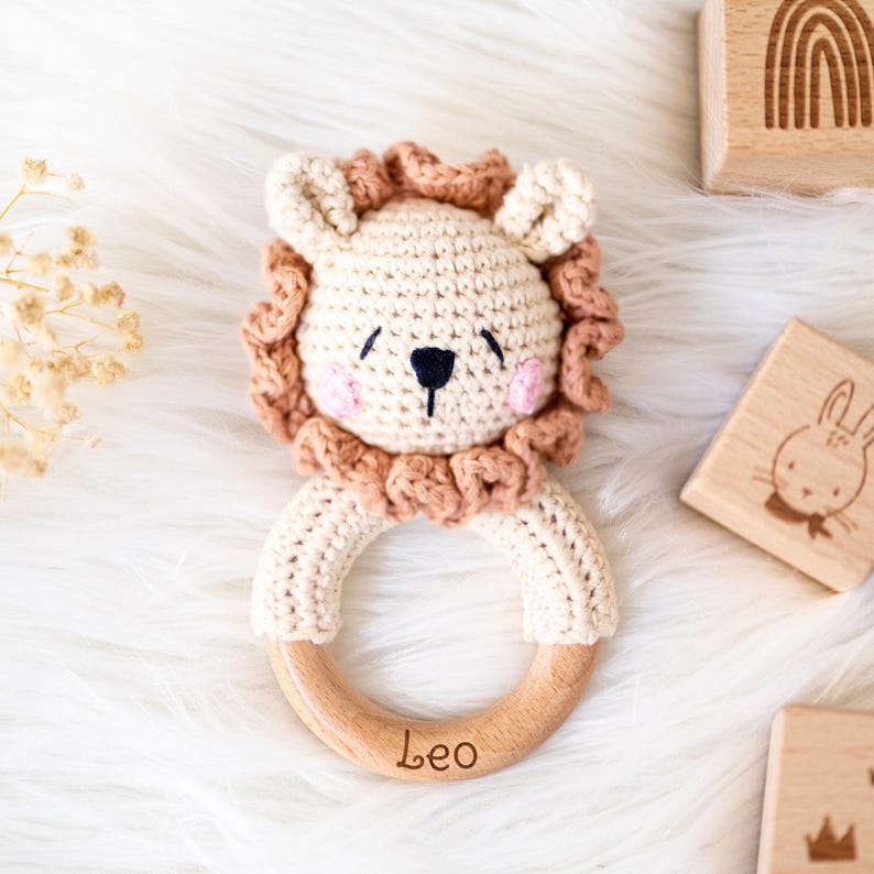 May include: A crocheted lion rattle with a wooden ring. The ring is engraved with the name "Leo".