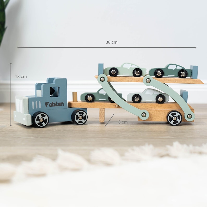 May include: A blue wooden toy truck with the name "Fabian" on the side, carrying four light green toy cars on a double-decker trailer. The truck is 13 inches long, 8 inches wide, and 38 inches tall.
