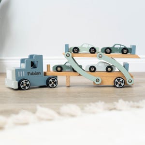 May include: A blue wooden toy truck with the name "Fabian" on the side, carrying four smaller blue wooden toy cars on a double-decker car carrier.