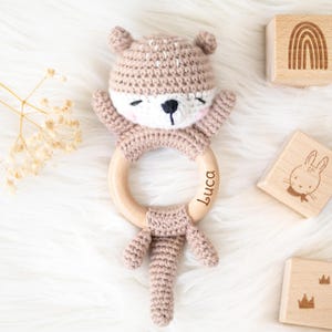 May include: A crocheted brown animal rattle with a wooden ring. The ring is engraved with the name "Luca".