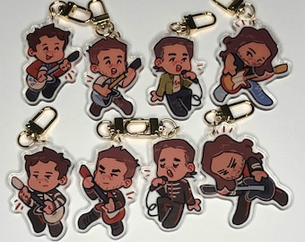 Peut inclure: Collection de porte-clés en acrylique représentant des musiciens de dessins animés jouant de la guitare et chantant. Chaque porte-clés a un fermoir doré. Les musiciens sont représentés dans diverses tenues, avec différentes coiffures et couleurs.