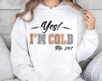 Może przedstawiać: Biała bluza z kapturem z czarnym napisem Yes! oraz Me 24:7, z wyrazami I'M COLD nadrukowanymi naprzemiennymi blokowymi literami w kolorze beżowym, szarym i jasnobrązowym. Odzież posiada przednią kieszeń typu kangurka oraz długie rękawy.