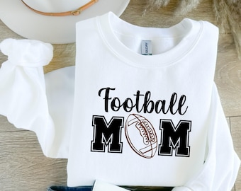 May include: White sweatshirt with black text that reads "Football Mom" and a brown football graphic.