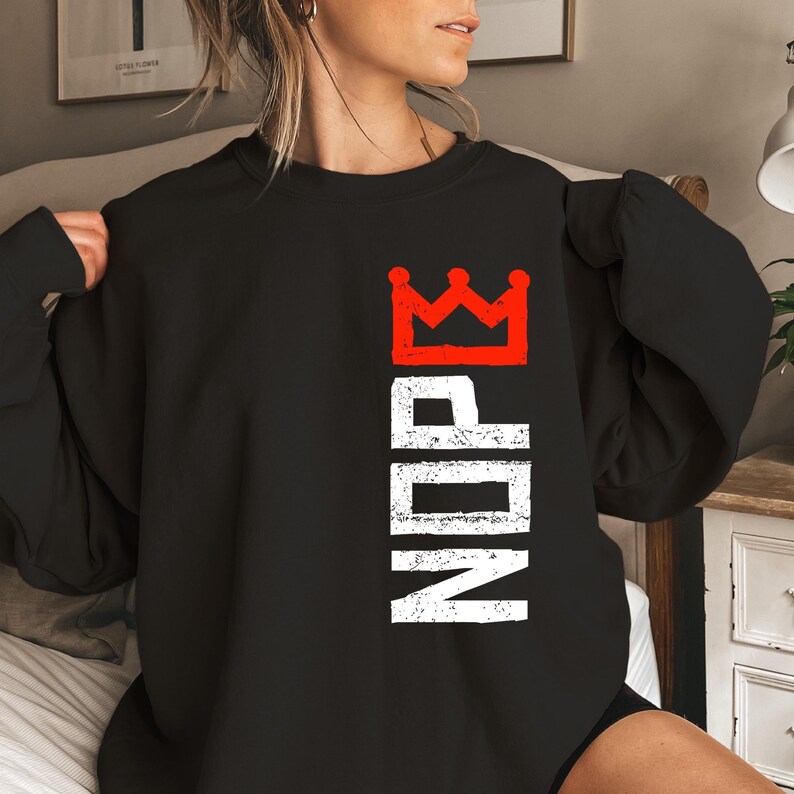 May include: Black crewneck sweatshirt with a red crown graphic above the word "NOPE" in white, vertically aligned. The design has a distressed, vintage look. The sweatshirt is a casual top.