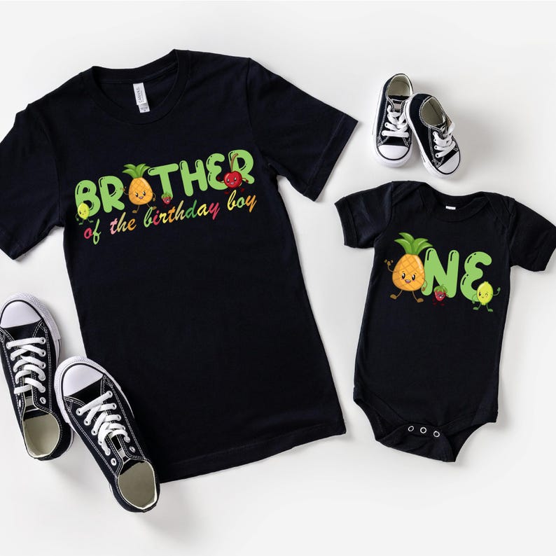 May include: Black t-shirts and a onesie with fruit graphics and text. The adult shirt says "Brother of the birthday boy" and the onesie says "ONE". Black and white sneakers are also in the image.