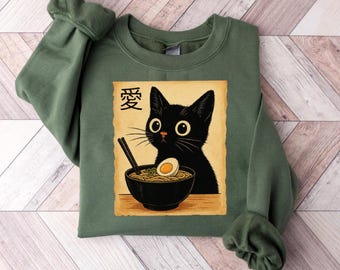May include: Green sweatshirt featuring a black cat with large yellow eyes, a bowl of ramen, and Japanese text. The cat is the focal point, with the ramen bowl below. The sweatshirt is a solid green color.