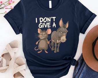May include: Navy blue t-shirt featuring a cartoon mouse holding a rope attached to a donkey. The text "I DON'T GIVE A" is printed above the animals. The shirt has a crew neck and short sleeves.