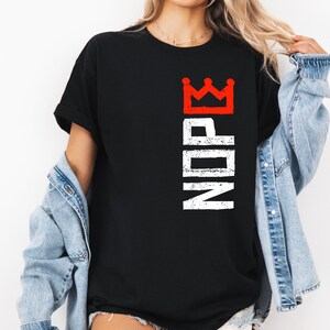 May include: Black t-shirt with a red crown graphic above the white letters "NDRE" printed vertically. The shirt is a classic crew neck style.