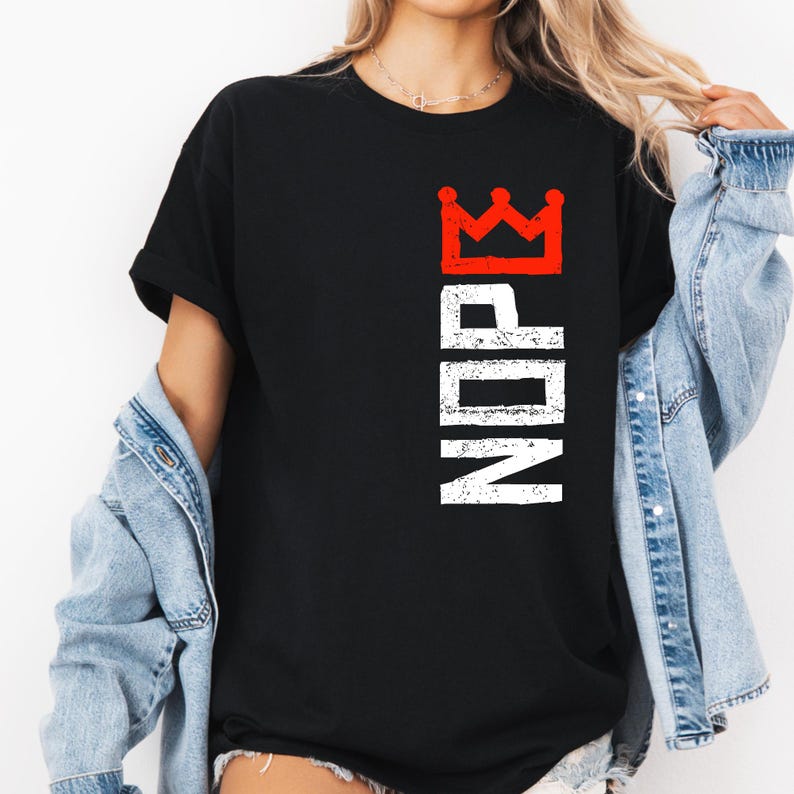 May include: Black t-shirt with a red crown graphic above the white letters "NDRE" printed vertically. The shirt is a classic crew neck style.