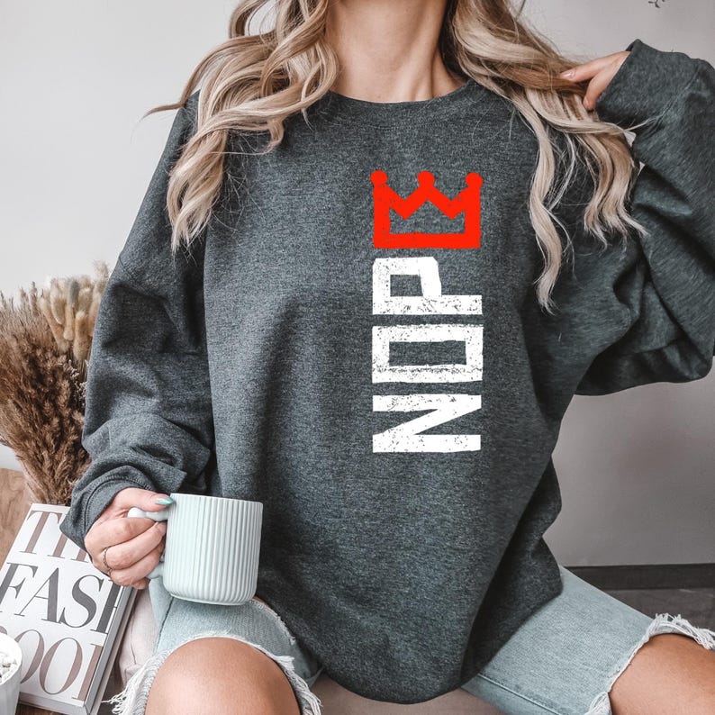 May include: Dark gray sweatshirt with the word "NDP" in white vertical text and a red crown graphic above. The sweatshirt is a crew neck style.