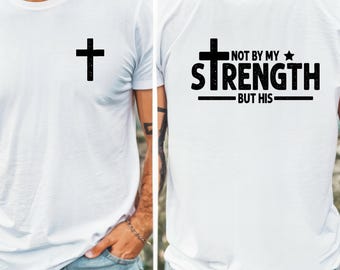 May include: White t-shirt with a black cross on the front and the text "NOT BY MY STRENGTH BUT HIS" on the back. The shirt is a crew neck and appears to be made of a soft material.