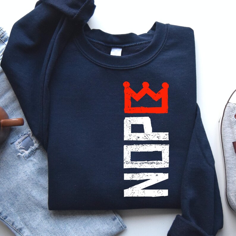 May include: Navy blue sweatshirt with the word "NOPE" in white vertical text and a red crown graphic. The sweatshirt is a casual garment, suitable for everyday wear.