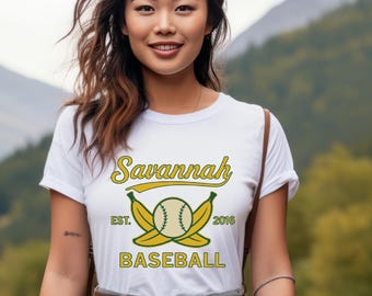 May include: White t-shirt with a baseball-themed graphic. The design features the word "Savannah" in yellow script above a baseball and crossed bananas, with "EST. 2016" and "BASEBALL" in yellow block letters.