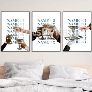 May include: Three framed prints featuring hands toasting with champagne glasses. Each print has a white background with blue text that reads "NAME #1", "NAME #2", and "NAME #3". The prints are displayed above a bed.