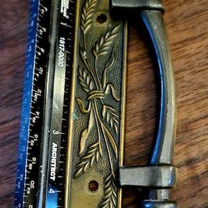 May include: Antique bronze door handle with wheat stalk design. The handle is 5 inches long and features a decorative plate with an embossed wheat pattern. The handle is a dark bronze color and has a curved grip.
