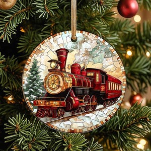 May include: Round Christmas ornament featuring a red and gold steam train design. The ornament has a stained glass effect with a train on tracks, a pine tree, and a gold hanging ribbon. The ornament is hanging on a Christmas tree.