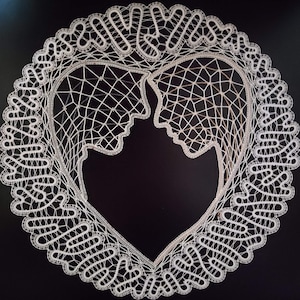 Könnte beinhalten: Eine weiße Spitzendecke mit einem herzförmigen Design, das zwei sich zugewandte Profile zeigt. Die filigrane Spitze ist vor einem schwarzen Hintergrund platziert und zeigt die filigrane Handwerkskunst und detaillierten Muster.