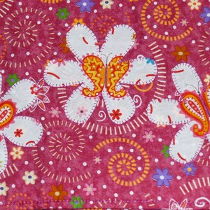 Könnte beinhalten: Nahaufnahme eines Stoffes mit sich wiederholendem Blumenmuster. Das Design zeigt große weiße Blumen mit orangefarbenen und gelben Paisley-förmigen Zentren auf einem tiefrosa Hintergrund mit kleineren Blumen und gepunkteten Details.