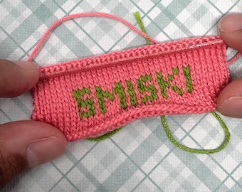 Könnte beinhalten: Nahaufnahme eines gestrickten rosa Stoffes mit dem Wort "BRIGHTS" in grüner Wolle gestickt.