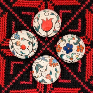 May include: Four round glass tiles featuring colourful floral patterns. The tiles have a white background with green, blue, red and orange flowers and leaves.
