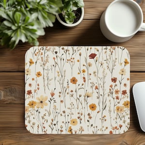 May include: A white mouse pad with a floral pattern featuring small yellow, orange, and red flowers on thin stems. The background is a light cream color.