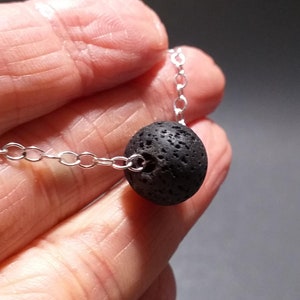 May include: A silver chain necklace with a black lava rock bead.