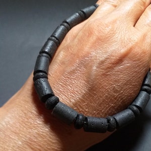 May include: A black lava rock bracelet with round beads. The bracelet is worn on a person's wrist.