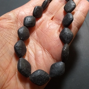 May include: A strand of black lava rock beads, each bead is a square shape with rounded edges.