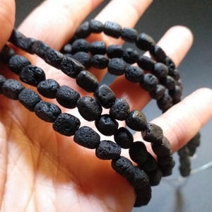 May include: A strand of black lava rock beads. The beads are round and have a rough, textured surface.