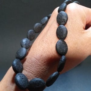 May include: A black lava rock bracelet with oval-shaped beads. The bracelet is worn on a person's wrist.
