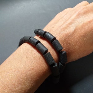 Könnte beinhalten: Ein schwarzes Armband aus zylindrischen Perlen. Das Armband wird am Handgelenk getragen.