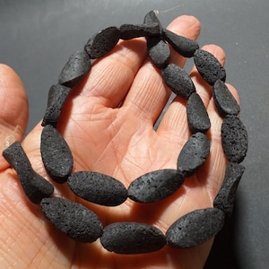 May include: A strand of black lava rock beads, oval shaped and slightly textured. The beads are strung on a clear thread.