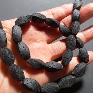 May include: A strand of black lava rock beads. The beads are oval shaped and have a rough, textured surface.