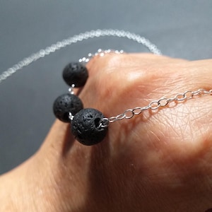 Könnte beinhalten: Eine silberne Kettenkette mit vier schwarzen Lavasteinen. Die Kette liegt auf einer Hand.