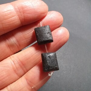May include: Two black square-shaped lava rock beads strung on a clear elastic cord.