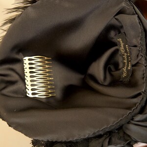 May include: A black satin headpiece with a gold comb and feather trim. The label reads "Melancholy Chapel, Made in France". The headpiece is likely vintage and suitable for special occasions.