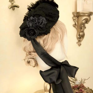 May include: A black hat with a floral design and feather accents. The hat features a large black bow and is displayed on a mannequin head. The hat is a vintage style.