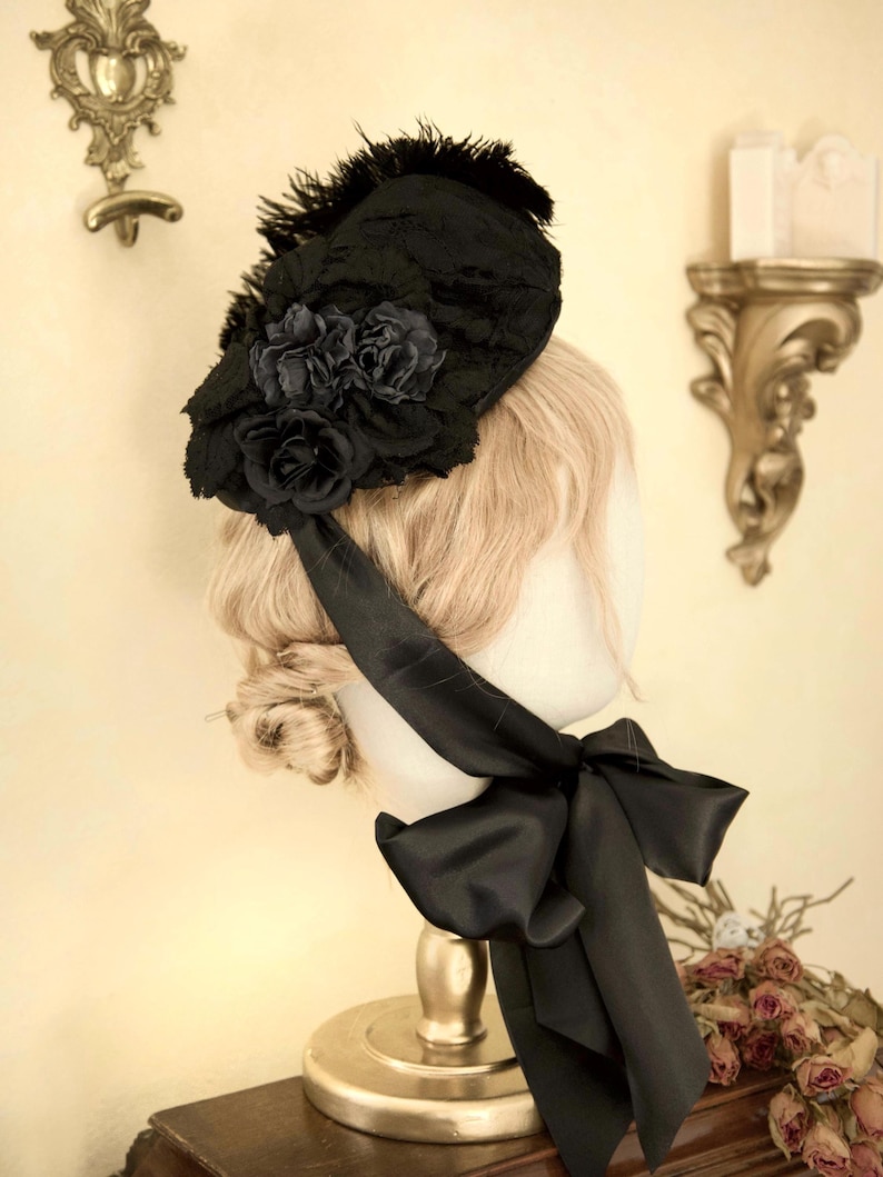 May include: A black hat with a floral design and feather accents. The hat features a large black bow and is displayed on a mannequin head. The hat is a vintage style.