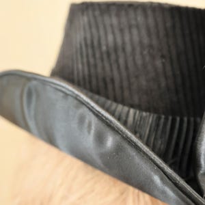 May include: A black top hat with a wide brim and a satin band. The hat is made of a textured fabric.
