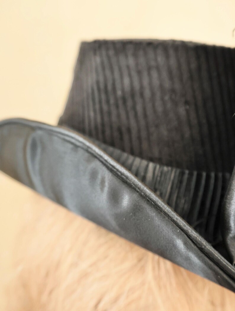 May include: A black top hat with a wide brim and a satin band. The hat is made of a textured fabric.