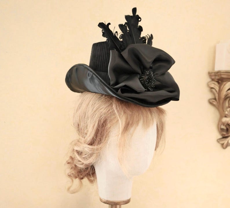 May include: A black hat with a wide brim and a large black bow on top. The hat is decorated with feathers and a black jewel.