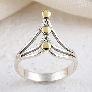 May include: A silver ring with three gold-colored spheres. The ring has a unique design with a layered, openwork structure. The gold spheres are evenly spaced along the top of the ring, adding a touch of elegance. The ring is likely made of sterling silver.