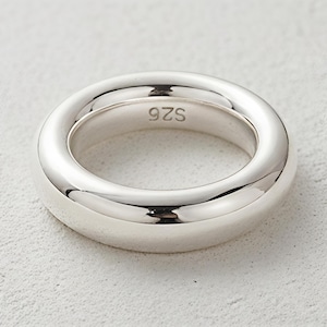 Puede incluir: Un anillo plateado brillante con un diseño liso y redondeado. El anillo tiene una banda gruesa y una superficie pulida, que refleja la luz. El texto "925" está estampado en el interior del anillo.